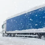 Big commercial semi-trailer truck trapped in snow drift on closed highway road at heavy snow storm blizzard cold winter day. Cargo vehicle stuck on freeway at bad weather conditions frosty snowfall